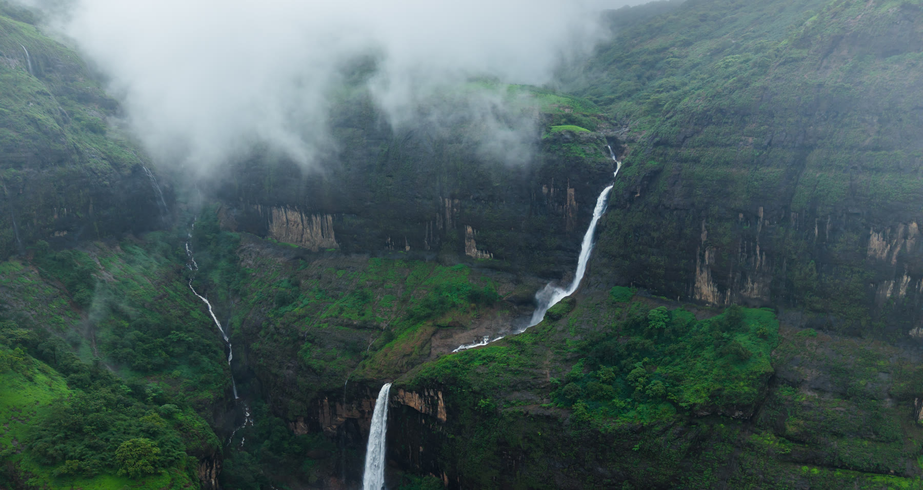 Colour-graded drone shot of a waterfall in misty green cliffs