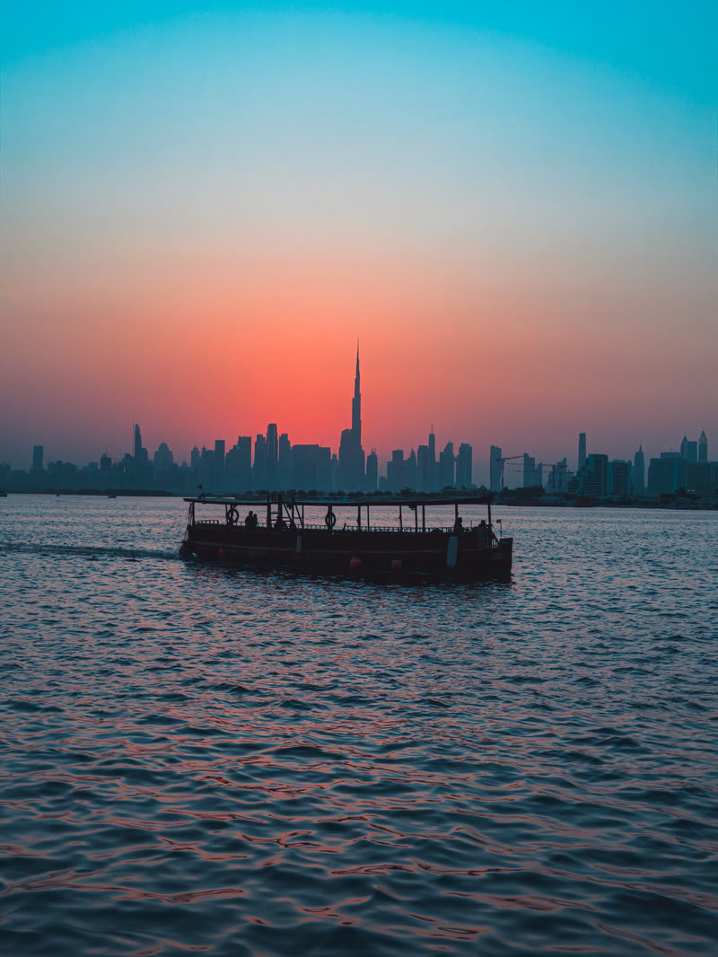 Boat crossing the water in front of the Dubai skyline at sunset