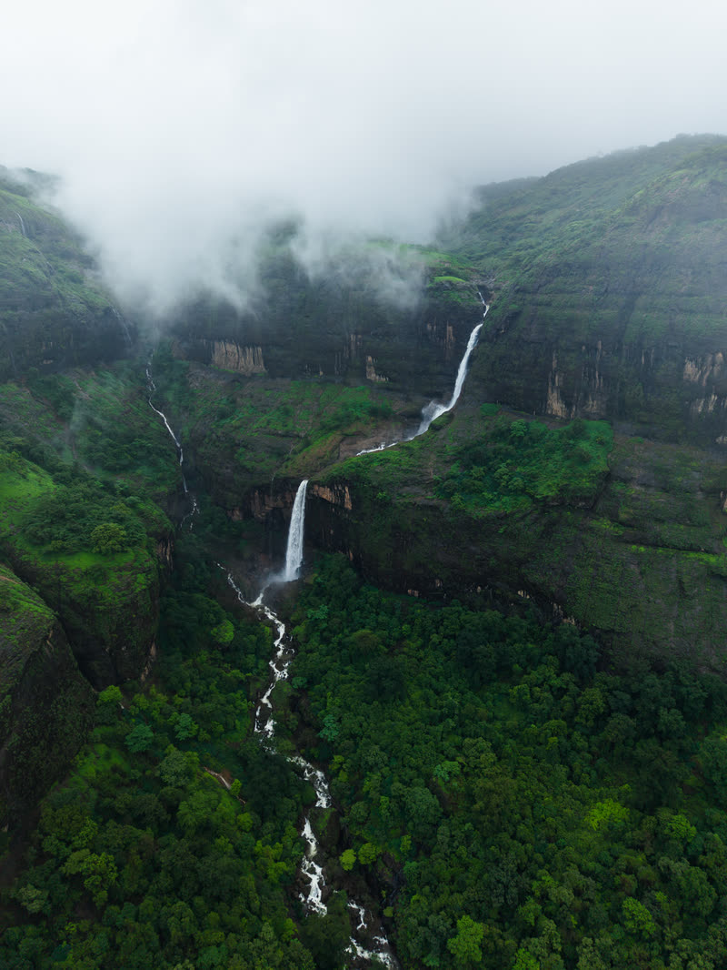 Waterfall cutting through green monsoon cliffs, from the drone