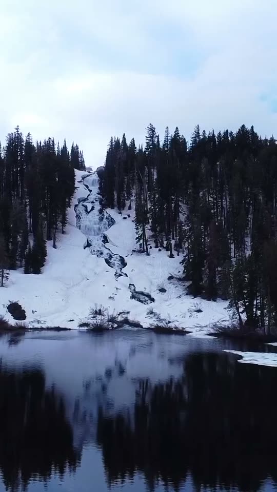 Snowy mountain lake reflecting pine trees